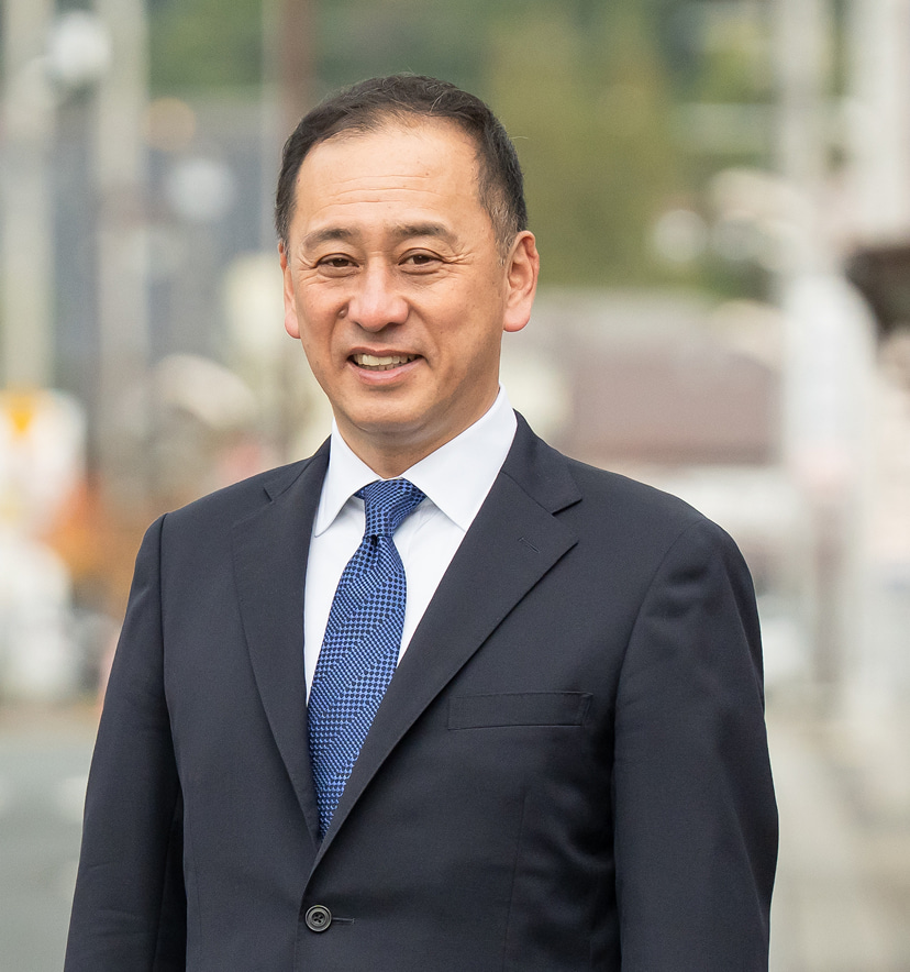 紫波町の風景を背景に、笑顔で立つ鎌田千市氏